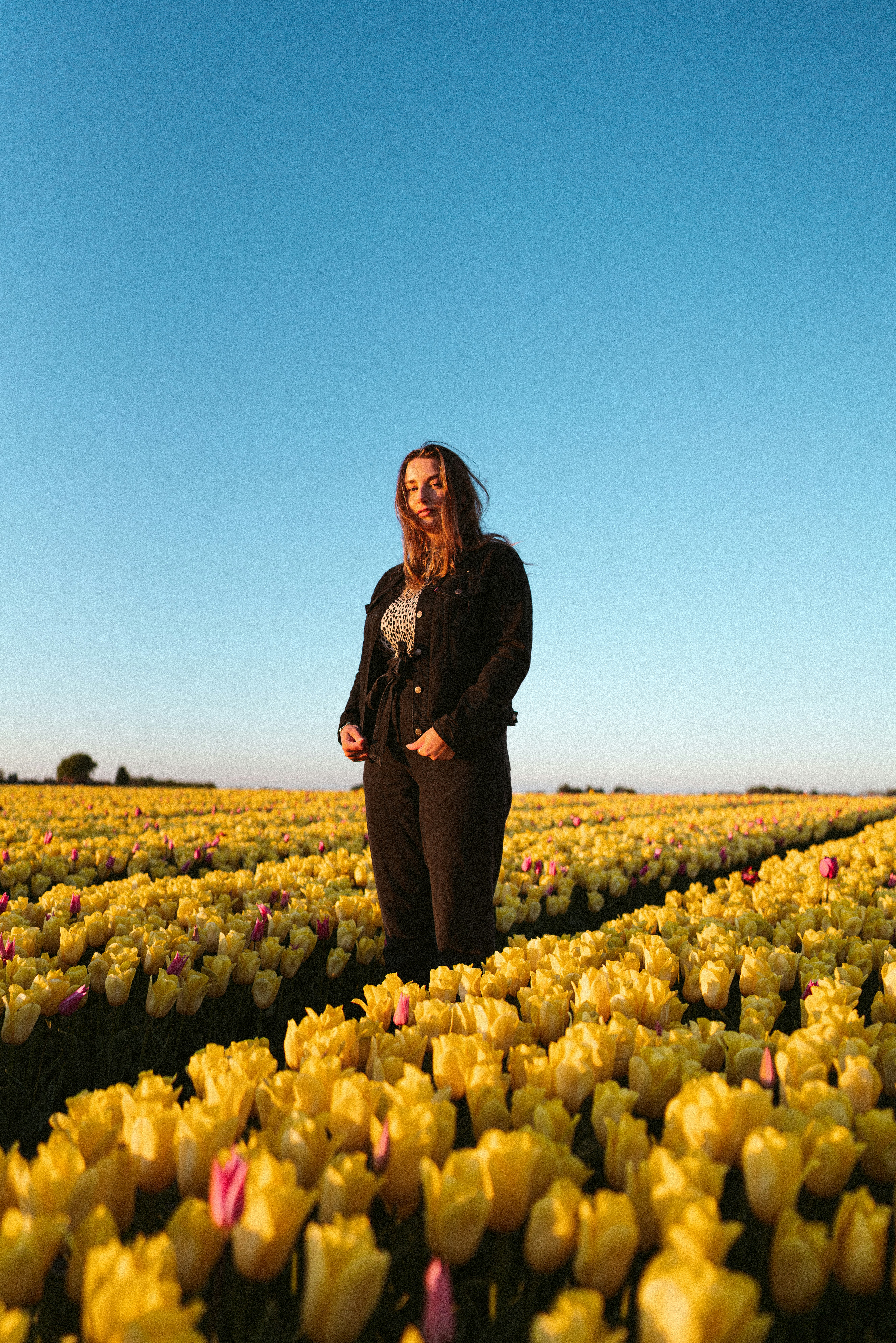 woman in black jacket standing on yellow flower field during daytime